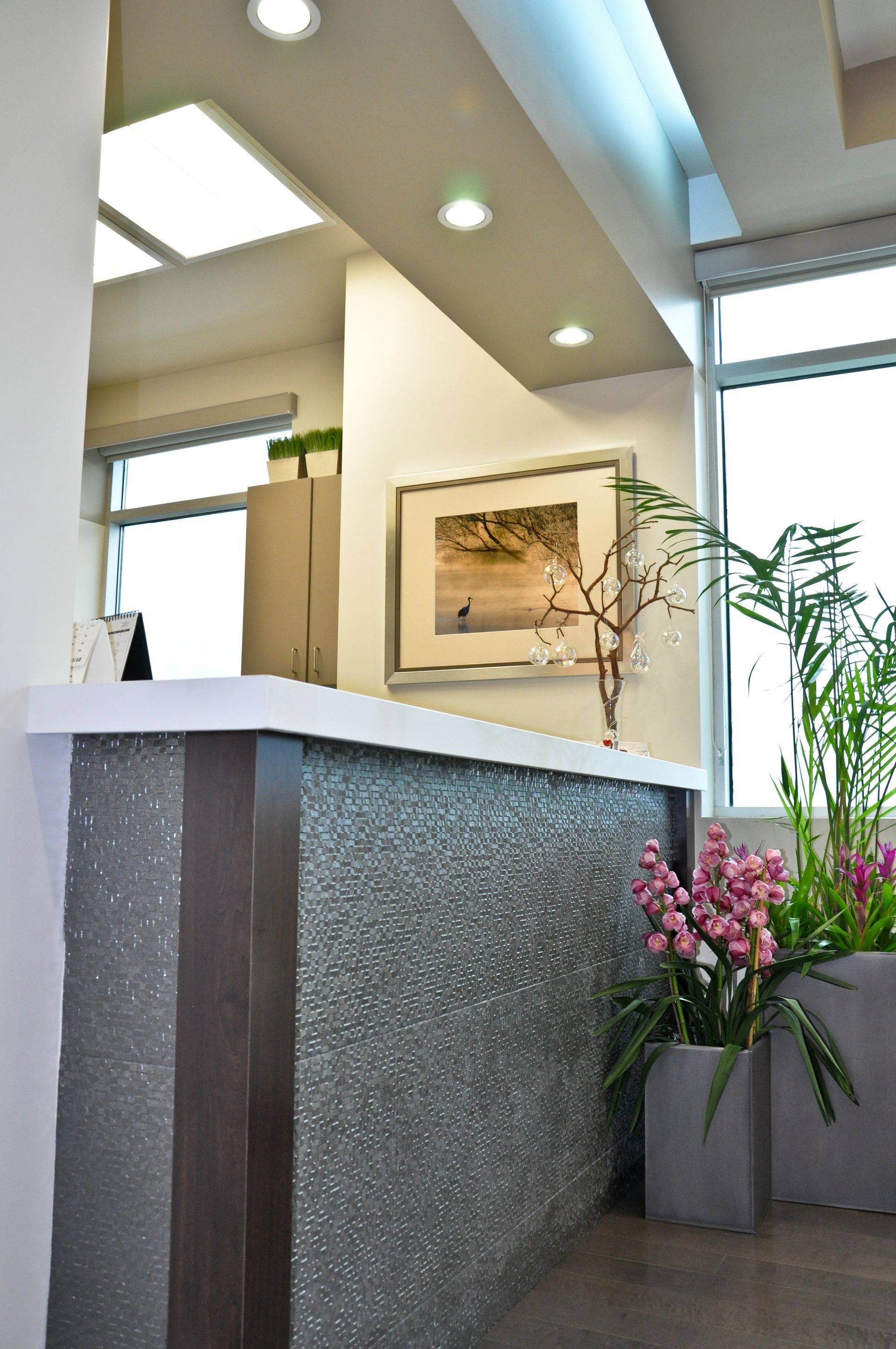 Reception desk in a modern office with textured gray facade, art, and potted plants.
