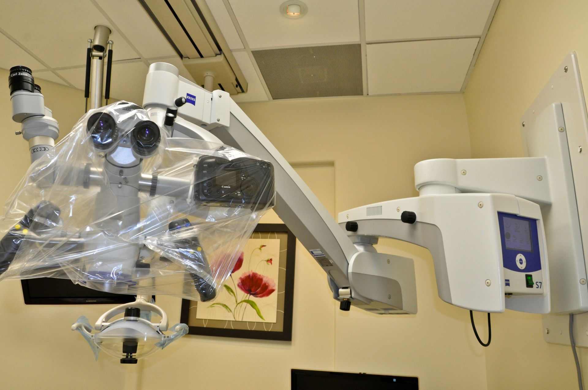 Dental surgical microscope mounted on a wall. White and gray device with protective covering, in a dental office.