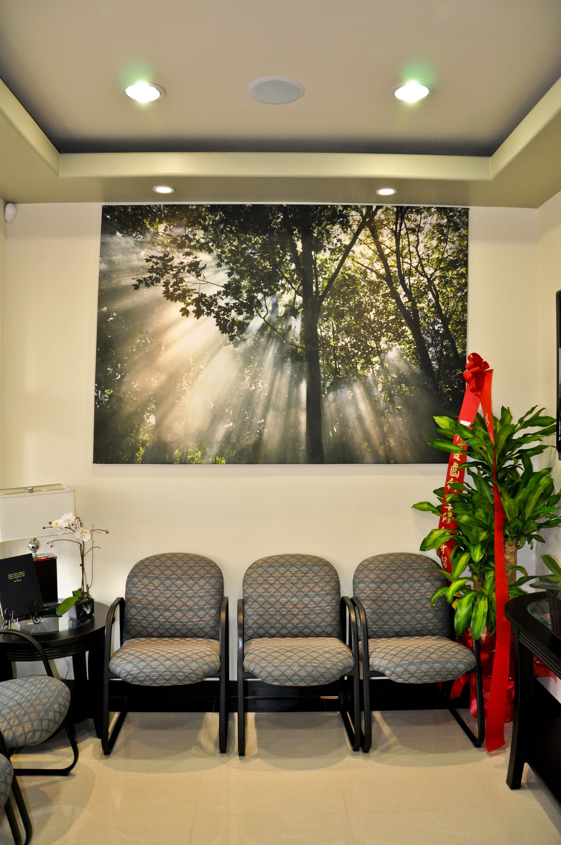 Waiting room with three gray patterned chairs under a forest scene painting.