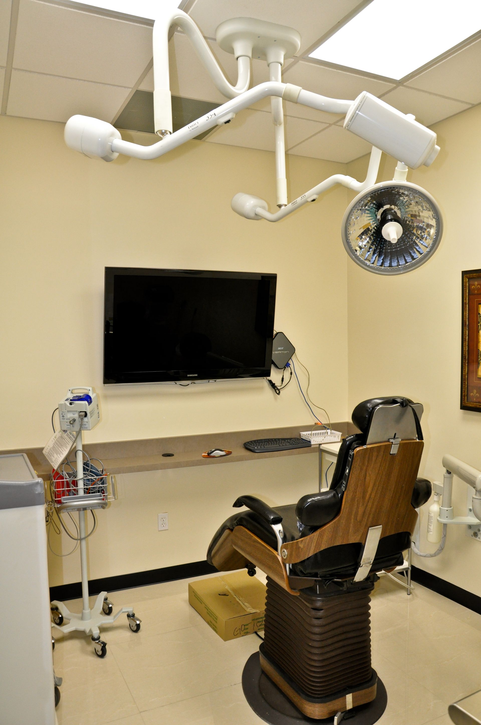 Dental examination room with chair, overhead light, and monitor.