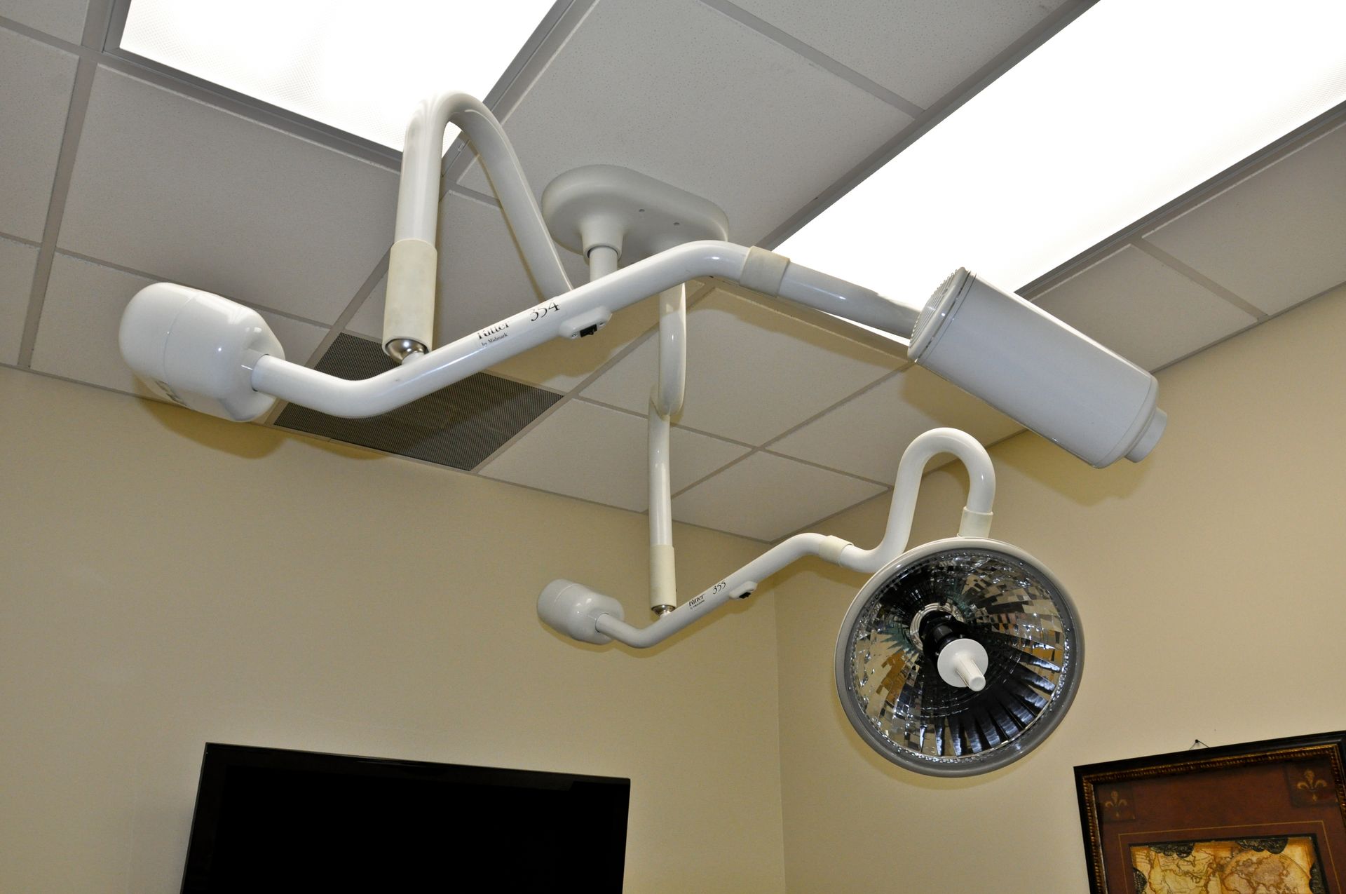 White medical exam lights hanging from the ceiling in a beige room.