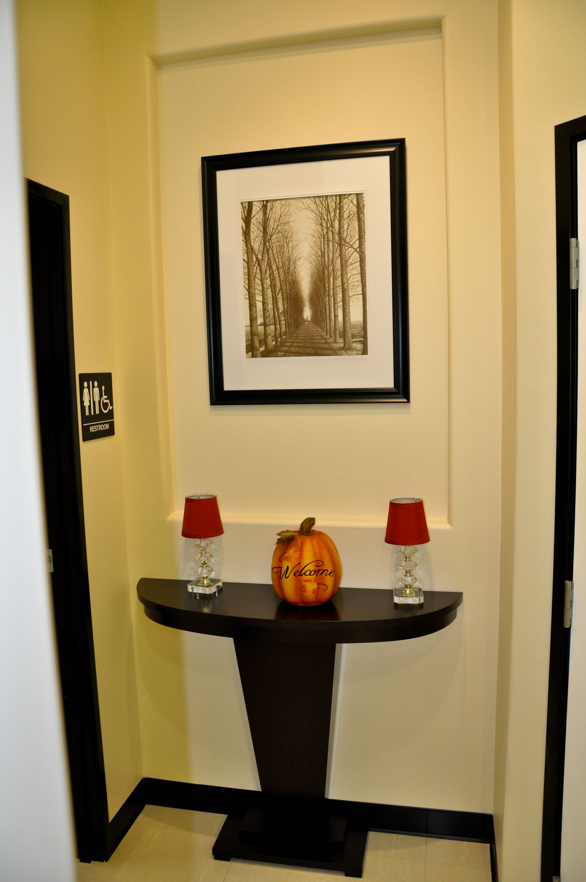Entryway with artwork above a console table holding lamps and a pumpkin.