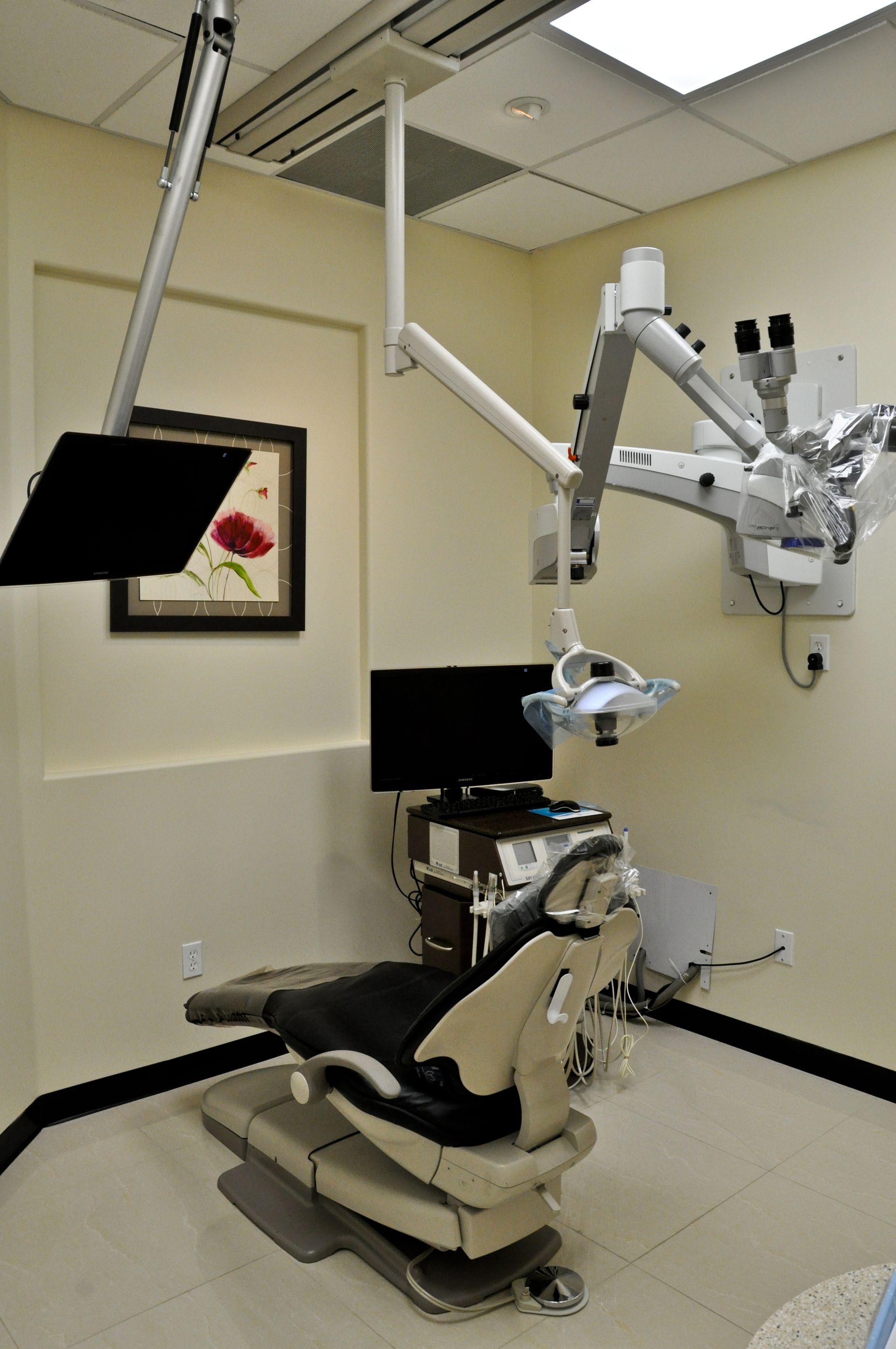 Dental office with patient chair, overhead microscope, and monitors.