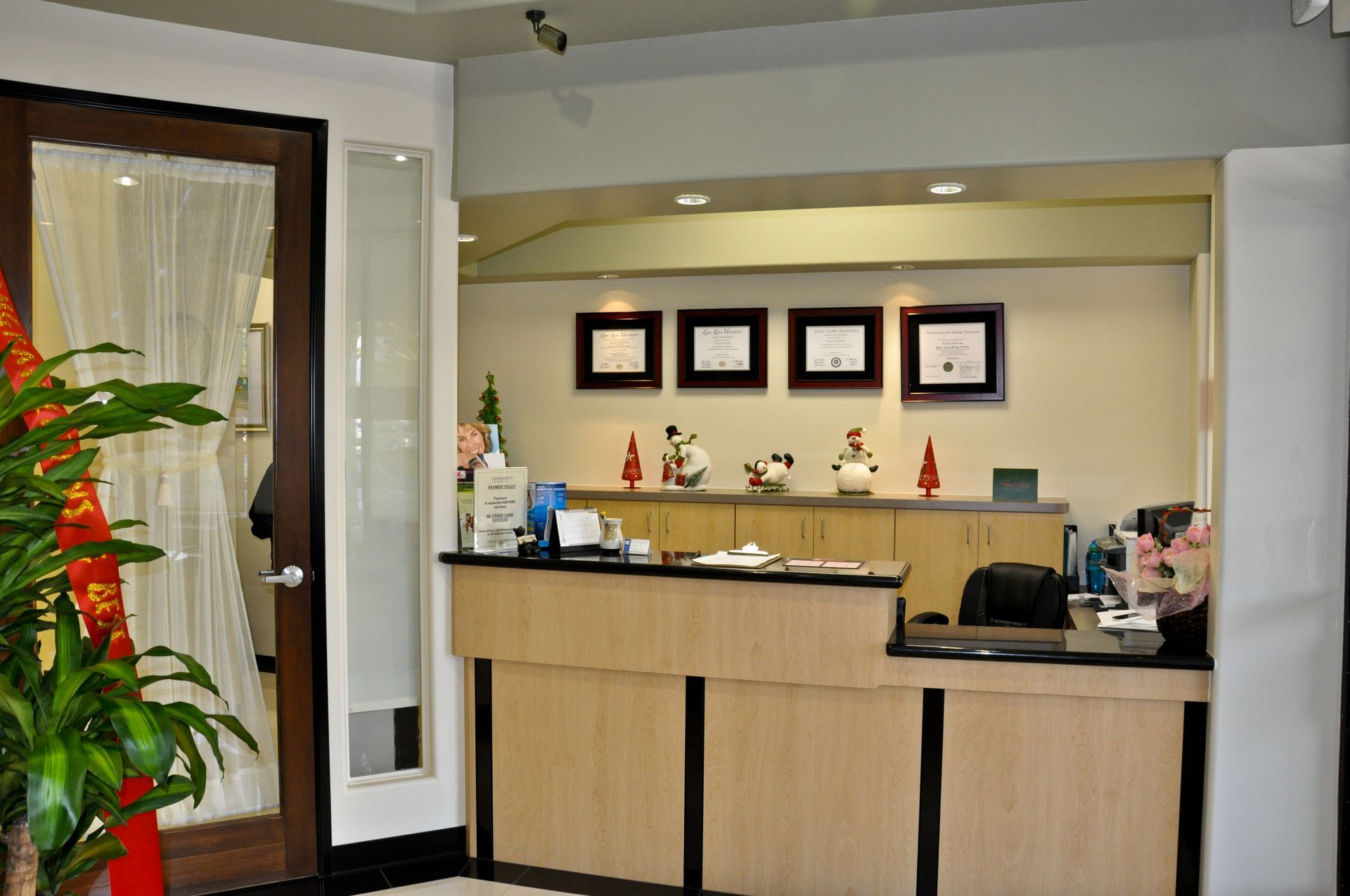 Reception desk in a bright office; wooden front, diplomas on the wall, decorative items.