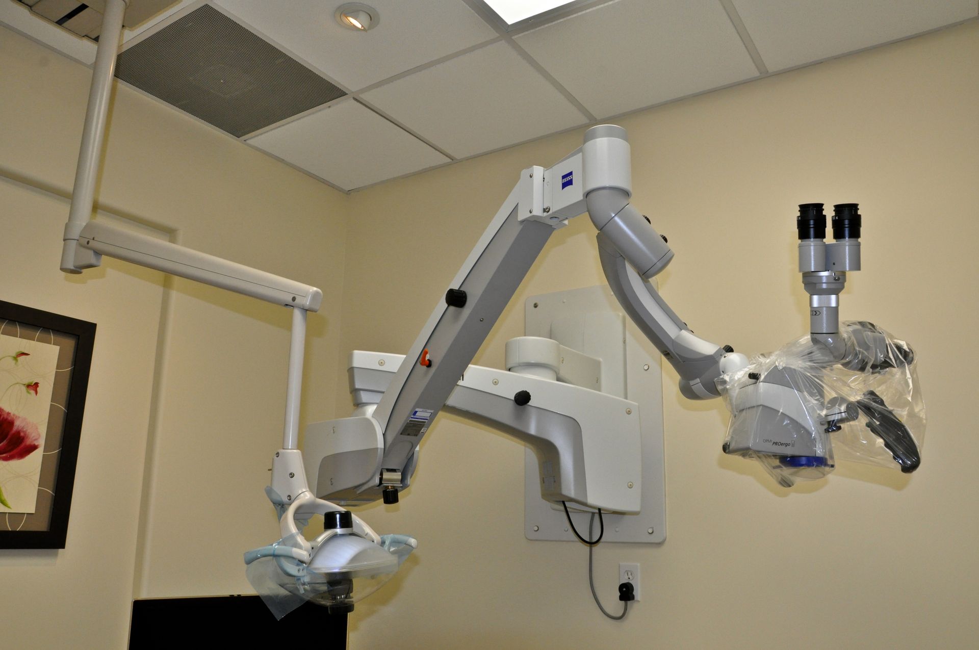 Wall-mounted surgical microscope in a cream-colored room; used in medical procedures.