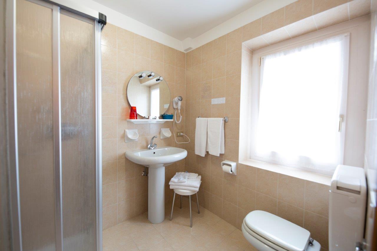 Piccolo bagno beige con doccia, lavabo a colonna, WC, finestra e portasciugamani.