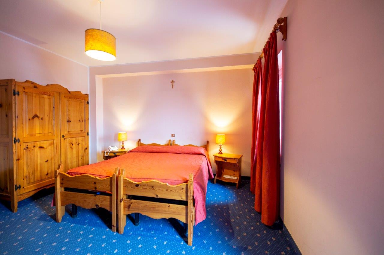 Accogliente camera da letto con letto in legno, copriletto rosa, armadio, lampade da comodino e tende rosse.