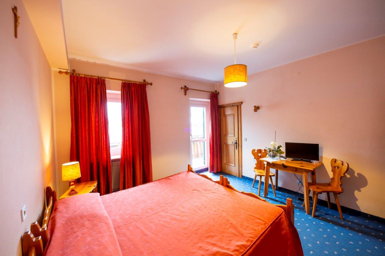 Camera d'albergo con copriletto arancione, tende rosse, scrivania, TV e tappeto blu.