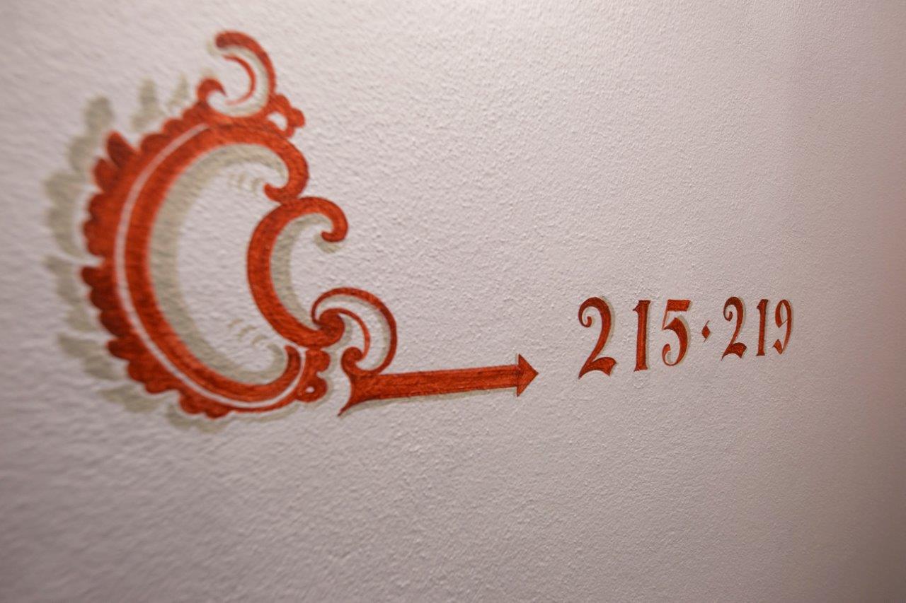 Etichetta decorata con freccia rosso-arancione che indica la gamma numerica da 215 a 219 su una parete bianca