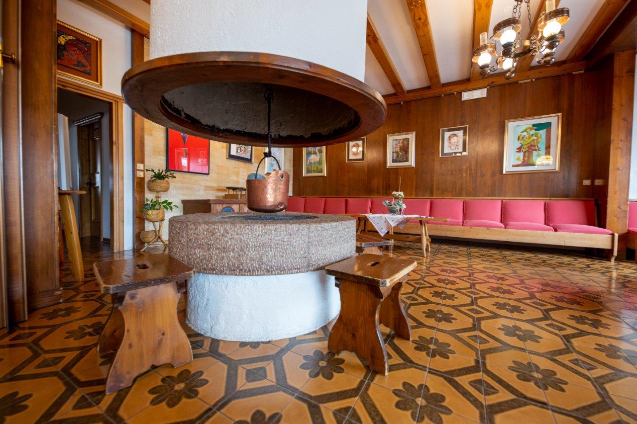 Atrio storico dell'hotel con fontana centrale in pietra, pavimento in piastrelle decorate, travi in legno e sedute rosa lungo la parete.