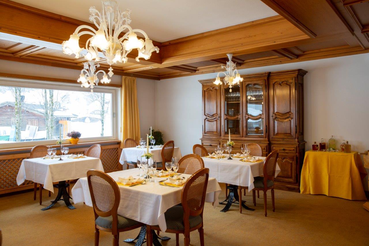 Elegante sala da pranzo di un ristorante con tovaglie bianche, lampadario e vetrina in legno.
