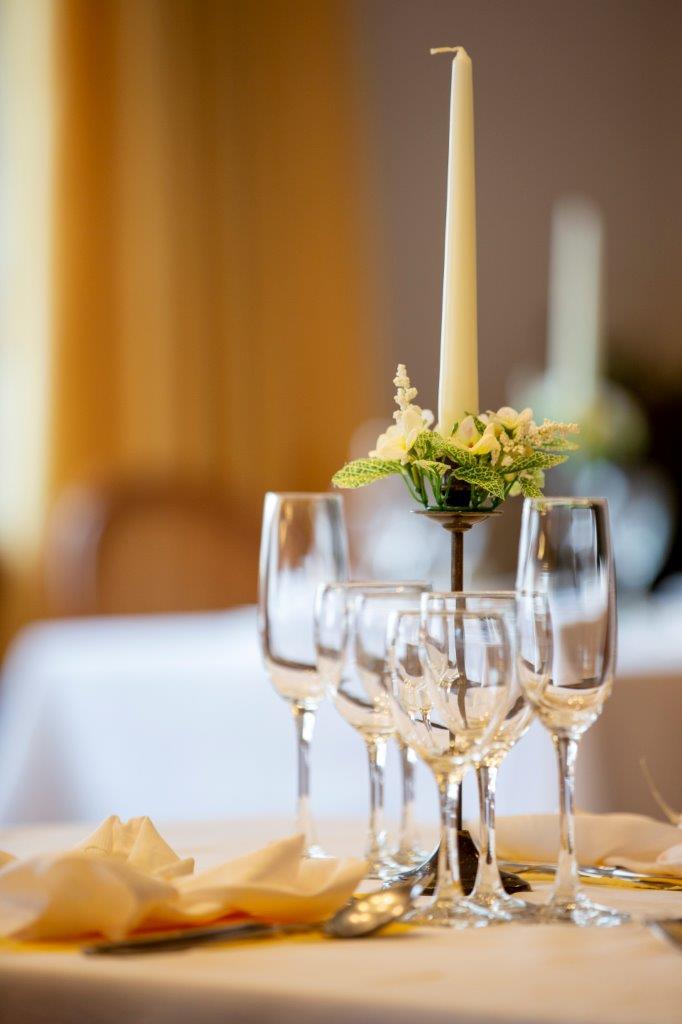 Allestimento del tavolo nuziale con candele bianche, calici da champagne e un centrotavola floreale su una tovaglia bianca.