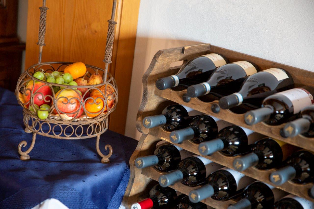 Portabottiglie accanto a un cesto di frutta decorativo su un tavolo ricoperto da una tovaglia blu.