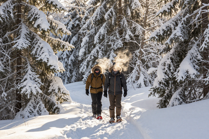 Due escursionisti camminano in una foresta innevata, ben coperti con abbigliamento invernale, con il respiro che si condensa nell'aria gelida.