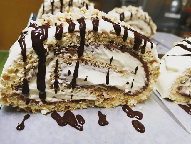 Fette di torta arrotolata alla crema, ricoperte di cioccolato e farcite con panna montata, disposte su un vassoio.