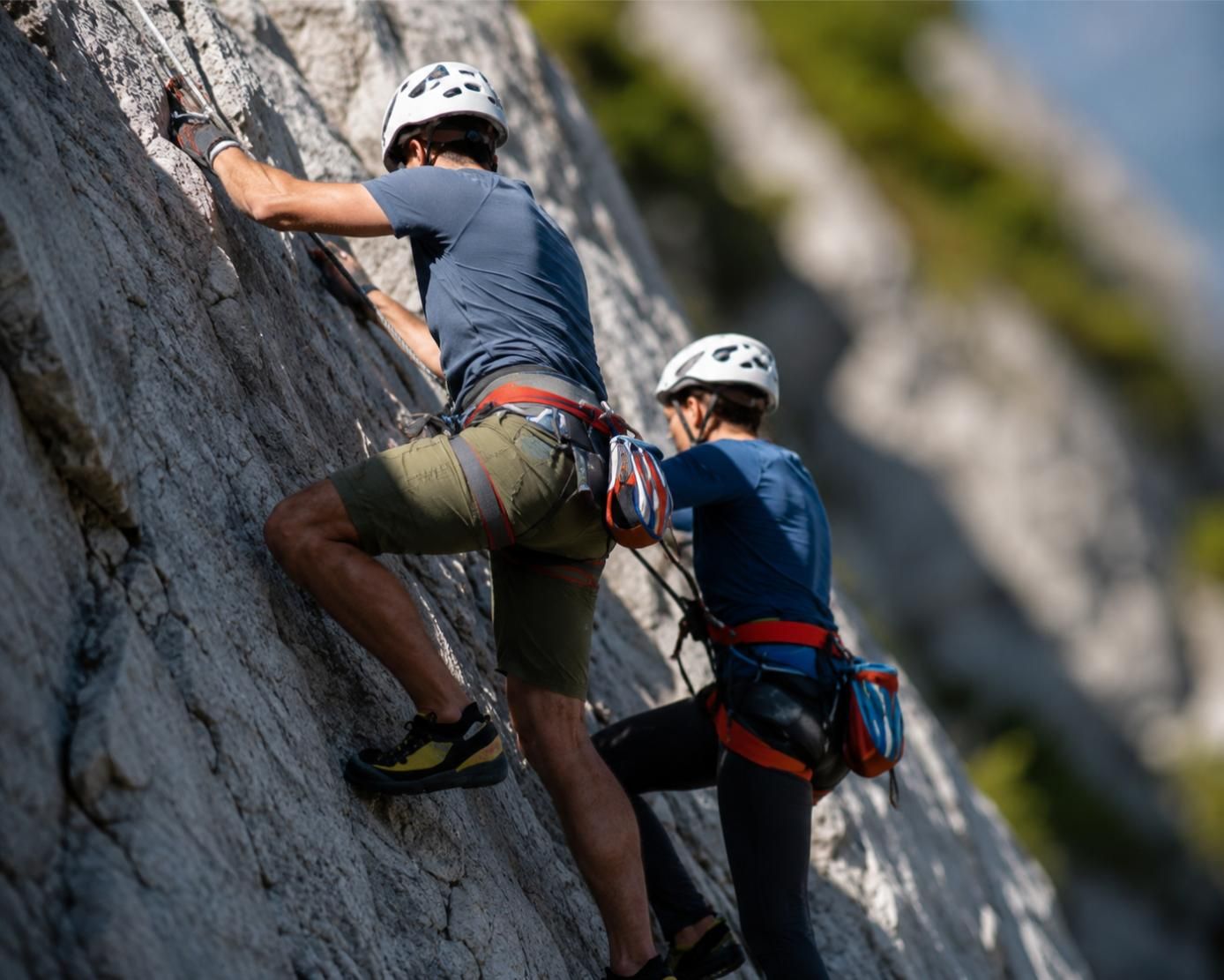 Due scalatori su una ripida parete rocciosa, con caschi e imbracature, mentre scalano una scogliera.