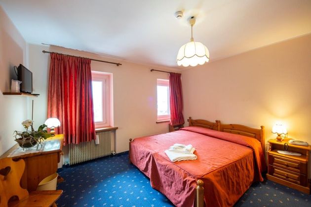 Accogliente camera da letto con letto matrimoniale, tende rosse, tappeto blu e lampada da comodino.
