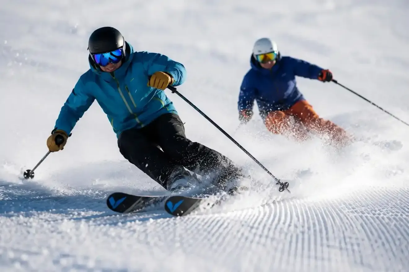 Due sciatori sfrecciano lungo un pendio innevato, sollevando nuvole di neve fresca.