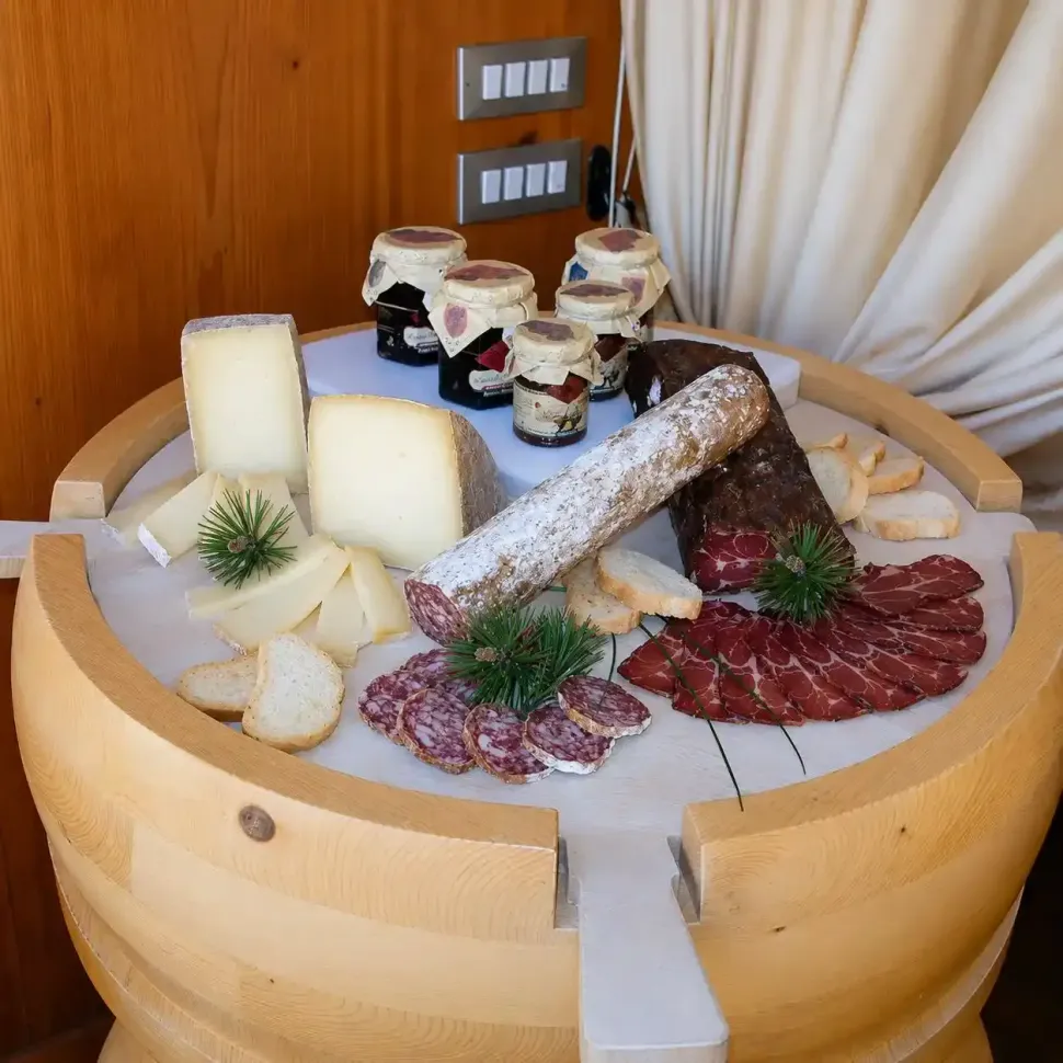 Piatto di formaggi e salumi su una botte di legno, con vasetti di salse e un'apparecchiatura rustica.