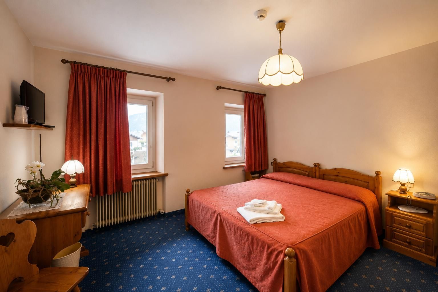 Accogliente camera da letto con tende rosse, letto matrimoniale, lampade da comodino e tappeto blu.
