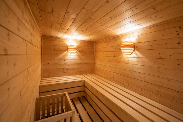 Interno della sauna rivestito in legno con panche e luci a parete a luce calda.
