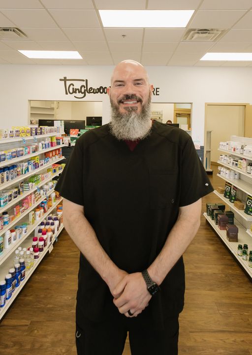 Smiling bald man with a long beard standing in an aisle of a store with shelves on both sides
