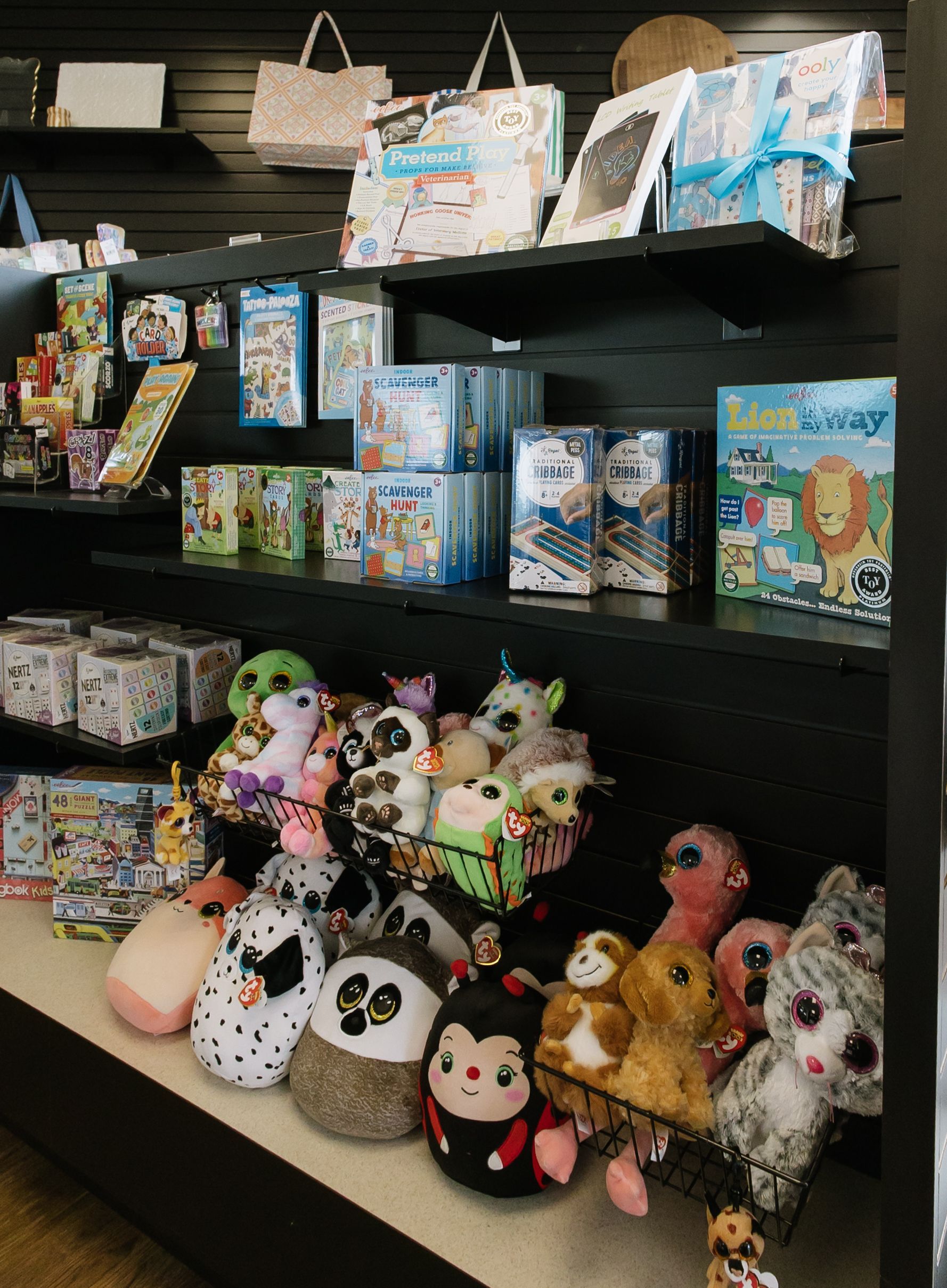 Store shelf filled with colorful plush toys, stuffed animals, and boxed gifts on black display shelves