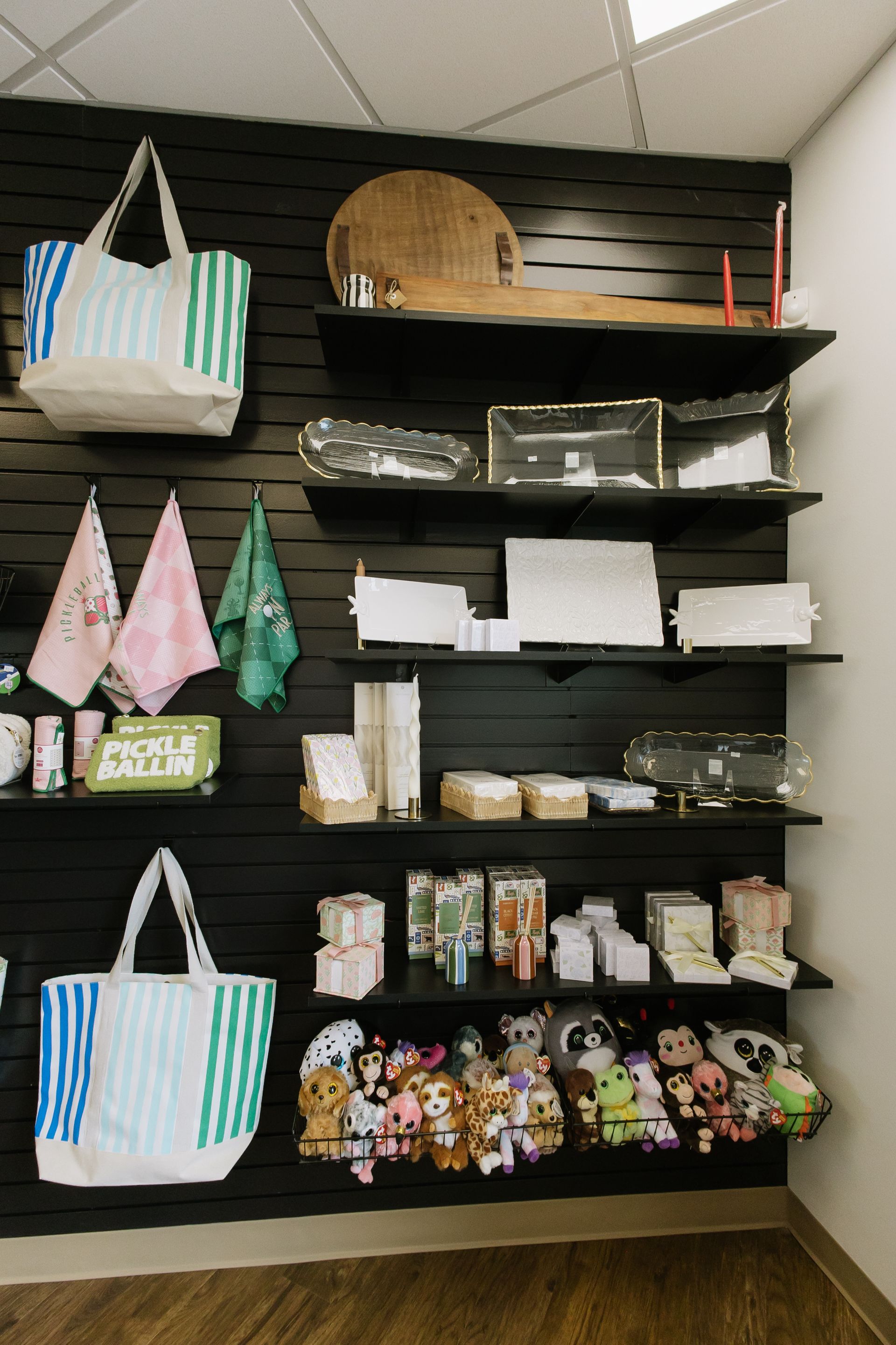 Retail display of floral handbags and pouches on black wall shelves with a wicker tote on top right
