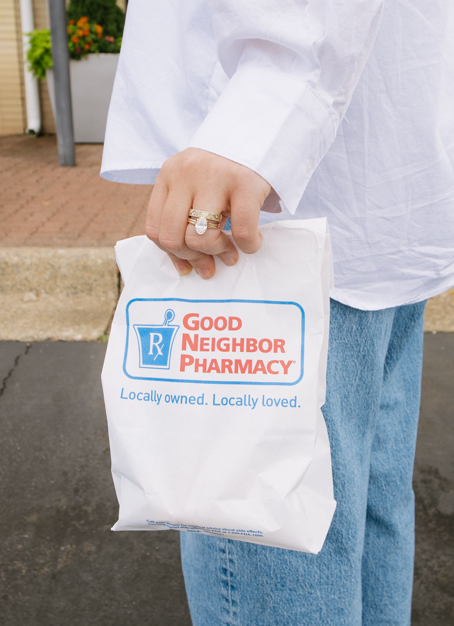 Person holding a white Good Neighbor Pharmacy shopping bag outdoors