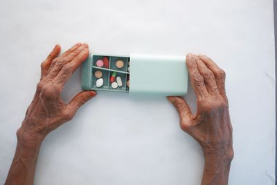 Hands holding open a mint-green pill organizer with assorted tablets on a white surface