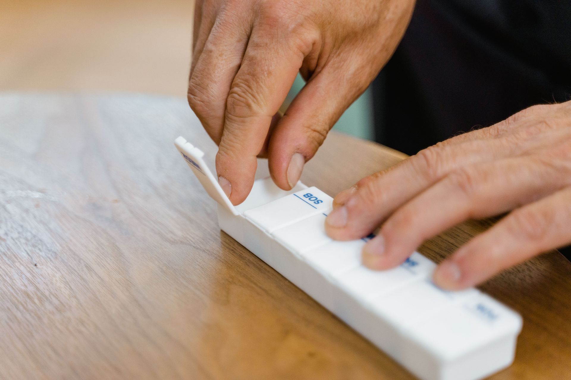 Hands using a white assistive device on a wooden table, pressing a button with a stylus.