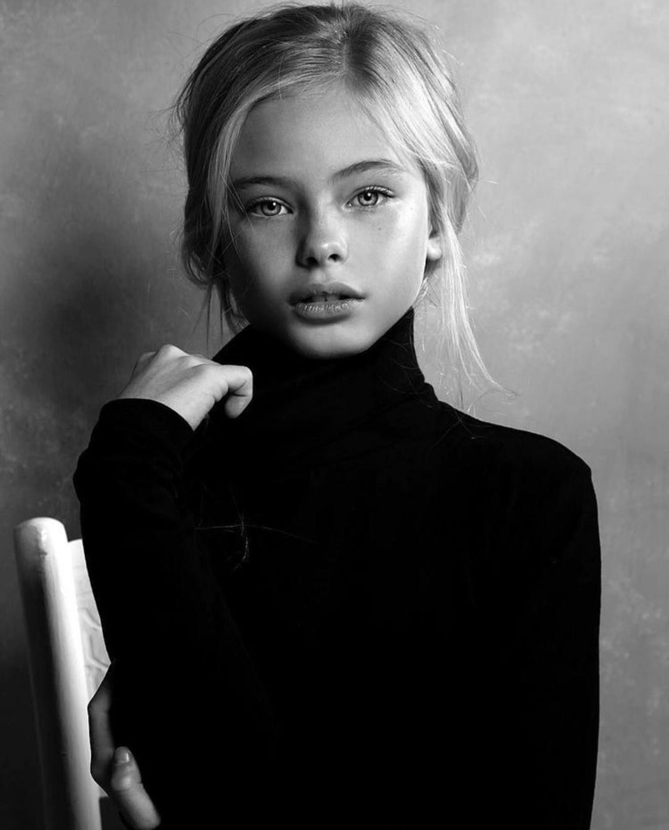 Blonde girl in black turtleneck, gazing directly at the viewer. Black and white photo.