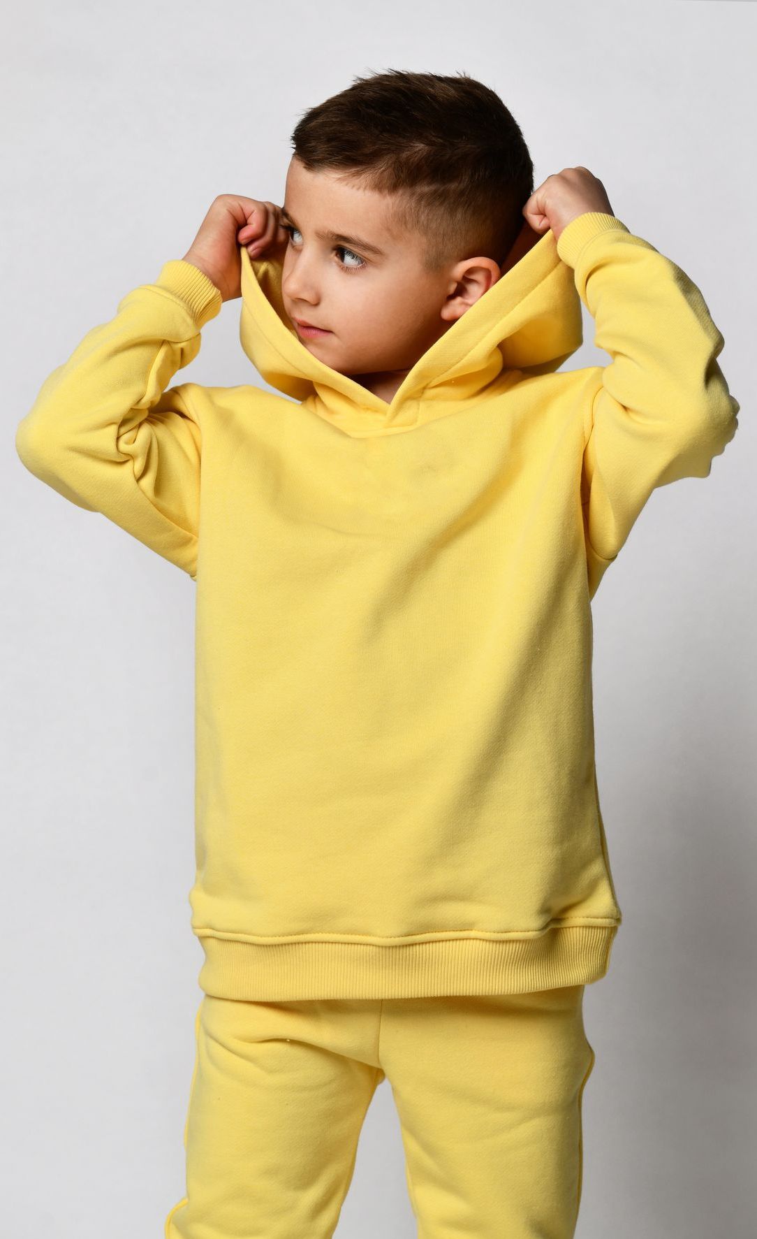 Boy in yellow hoodie and pants, pulling up the hood.