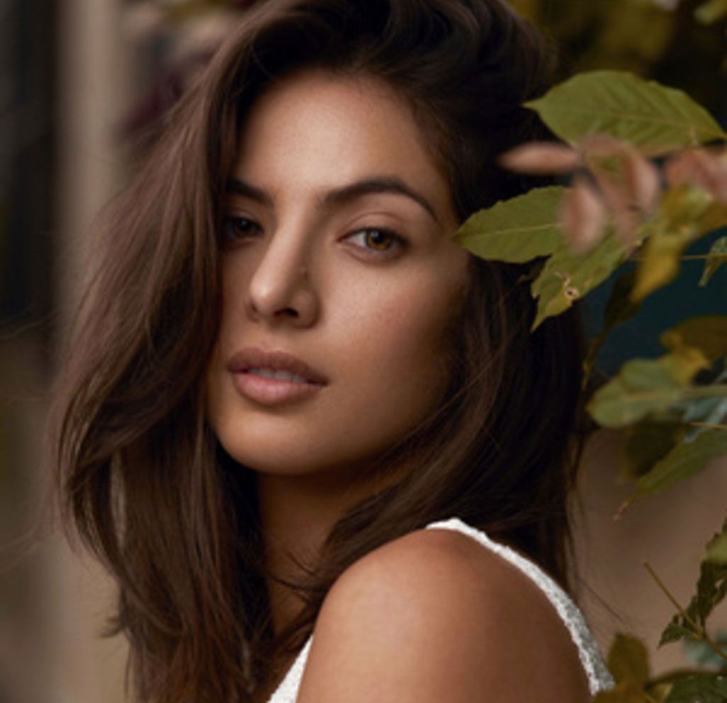 A close up of a woman 's face with leaves in the background