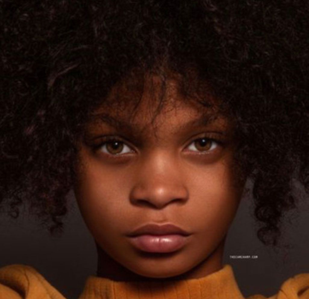 A young girl with curly hair is wearing a yellow sweater