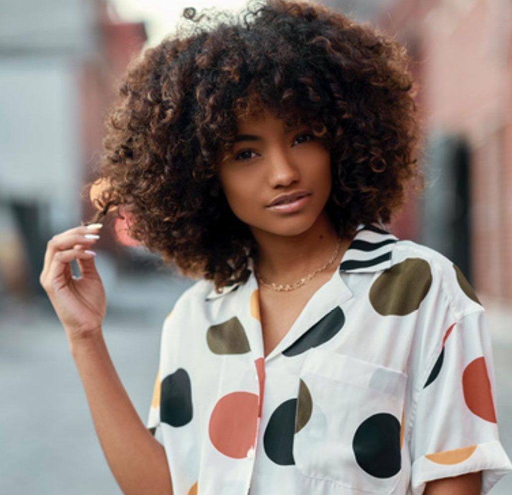 A woman in an orange sweater is standing in front of a yellow taxi