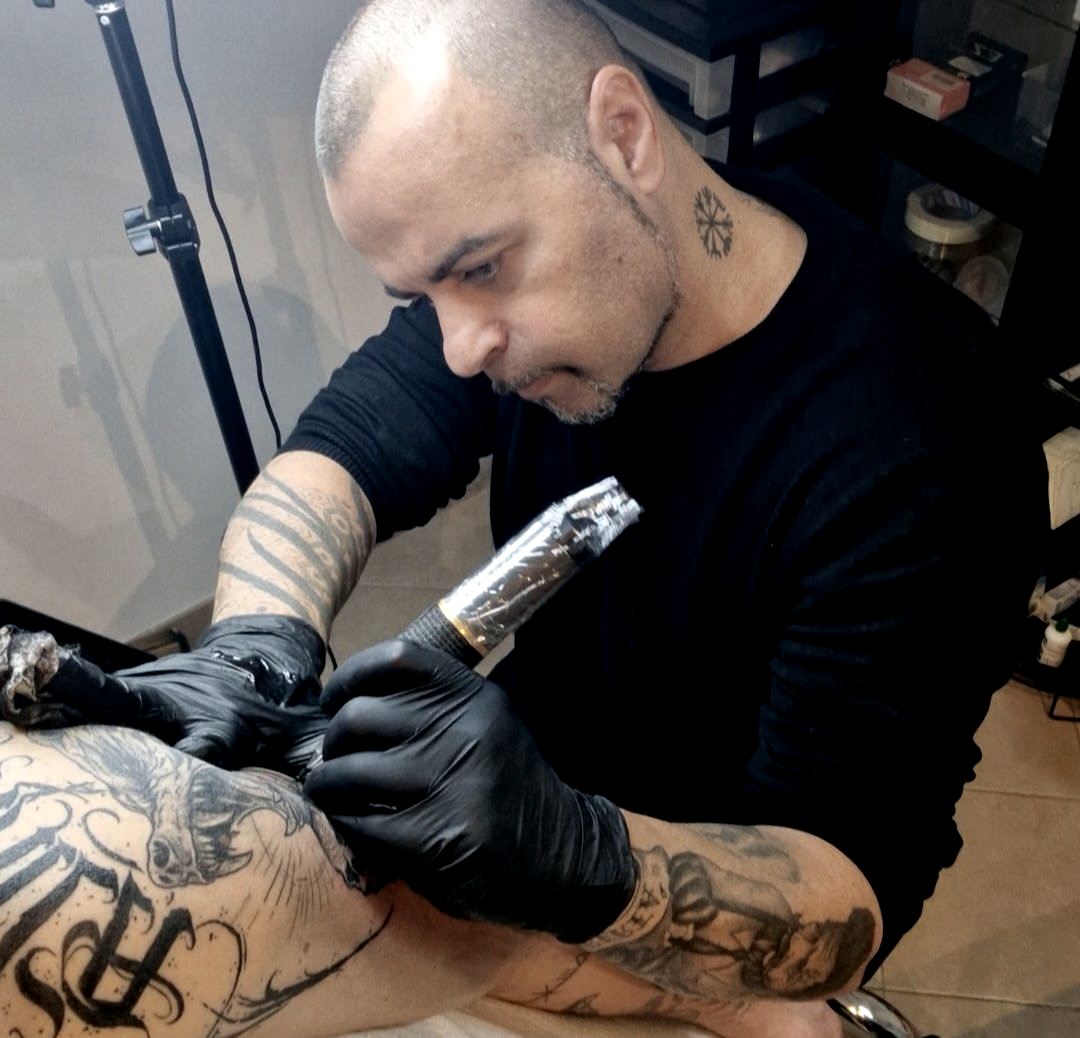 Un tatuatore con i guanti neri tatua il braccio di un cliente con una macchinetta in uno studio.