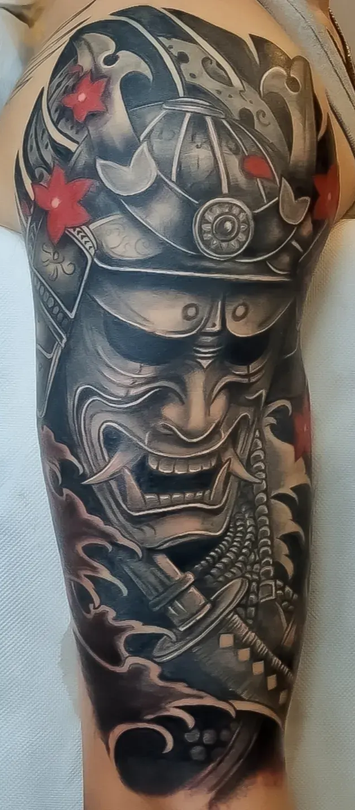 Elmo da samurai nero e grigio e tatuaggio di un guerriero feroce su un braccio