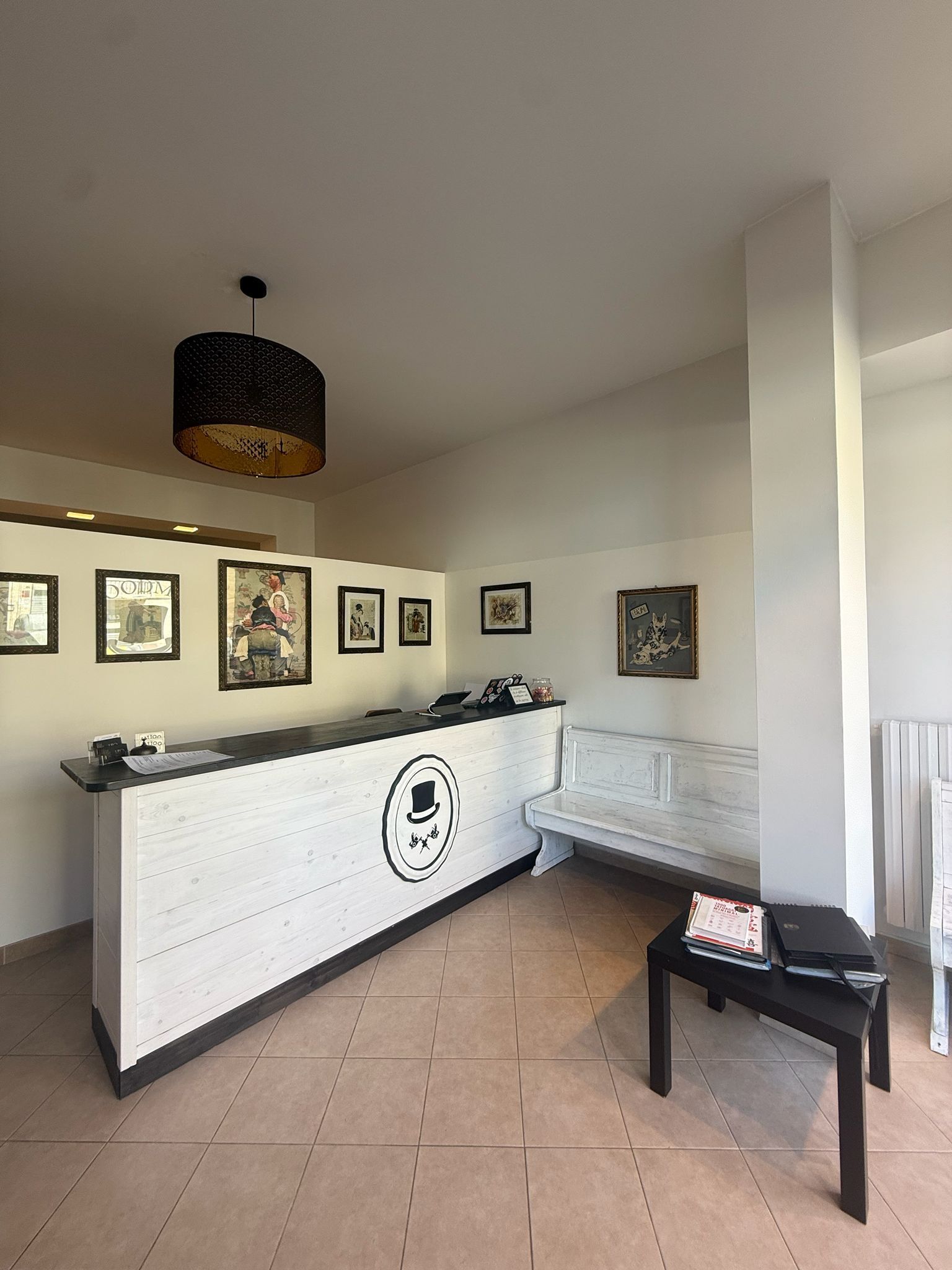 Piccola hall con bancone della reception, opere d'arte alle pareti, divano e tavolino nero sotto una lampada a soffitto.