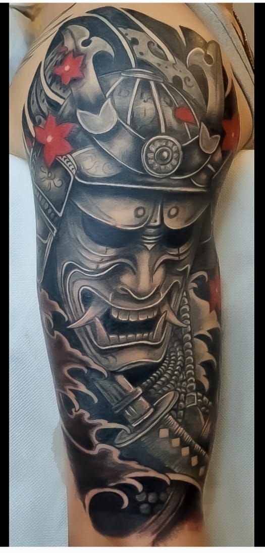 Avambraccio tatuato con una maschera da samurai scura e decorazioni a stella rossa
