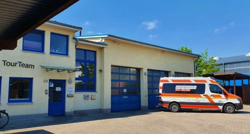 Außenansicht des Tourlean-Gebäudes mit blauem Garagentor und einem davor geparkten orange-weißen Krankenwagen.