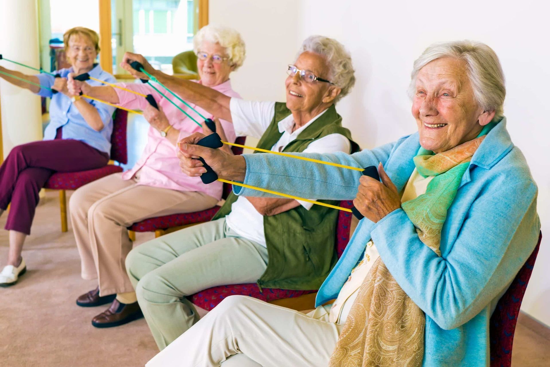 A group of elderly women are sitting in chairs doing exercises with resistance bands.