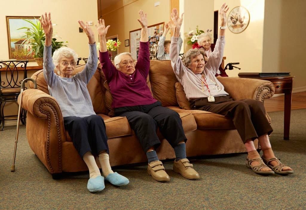 Three elderly women are sitting on a couch with their arms in the air