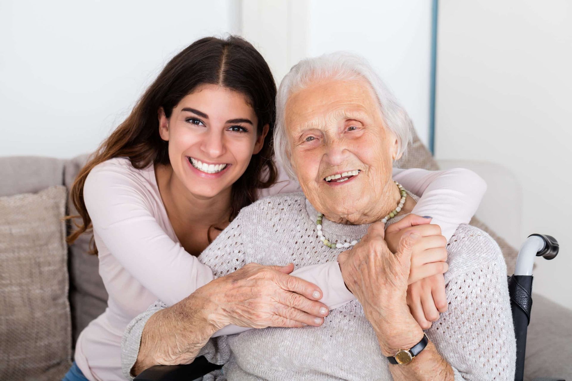 A young woman is hugging an older woman in a wheelchair.