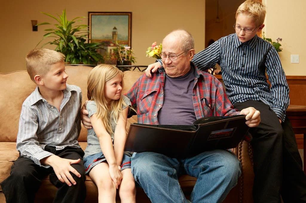 A family is sitting on a couch looking at a photo album.