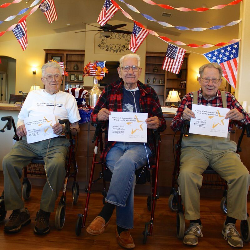 Three elderly men are sitting in wheelchairs holding papers