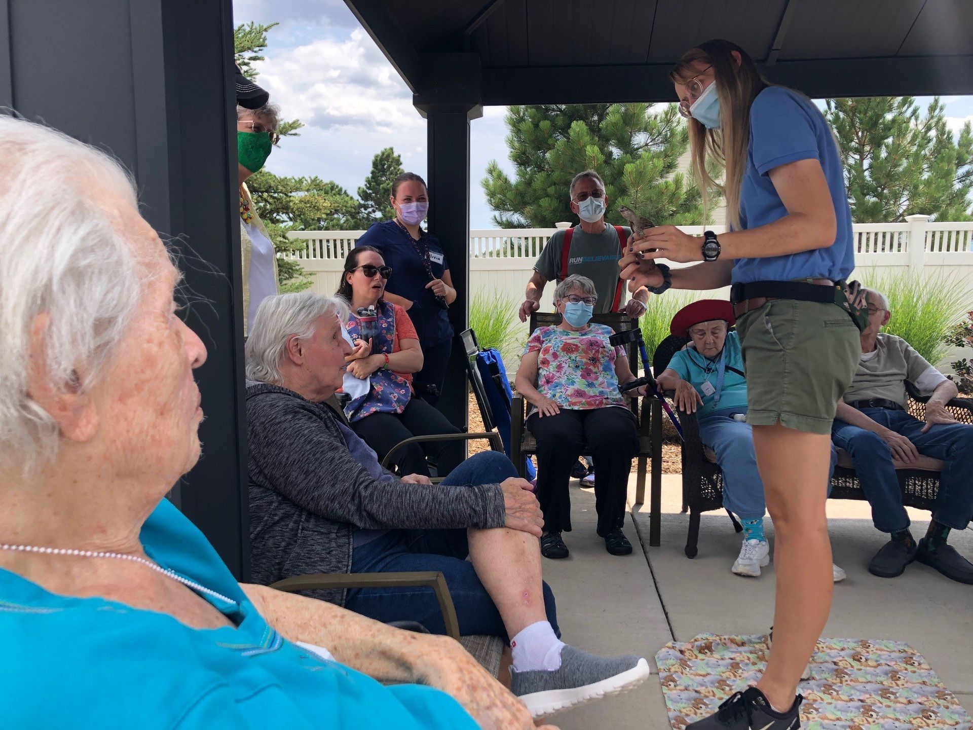 A woman wearing a mask is standing in front of a group of elderly people.