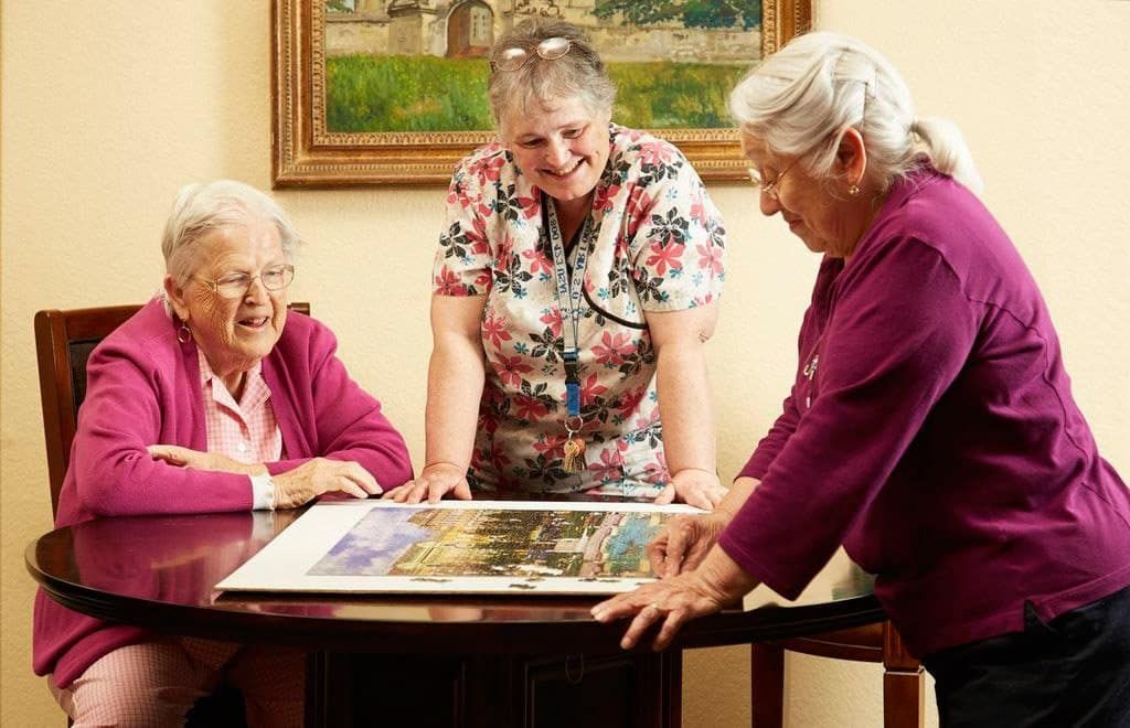 Three elderly women are sitting at a table looking at a picture.
