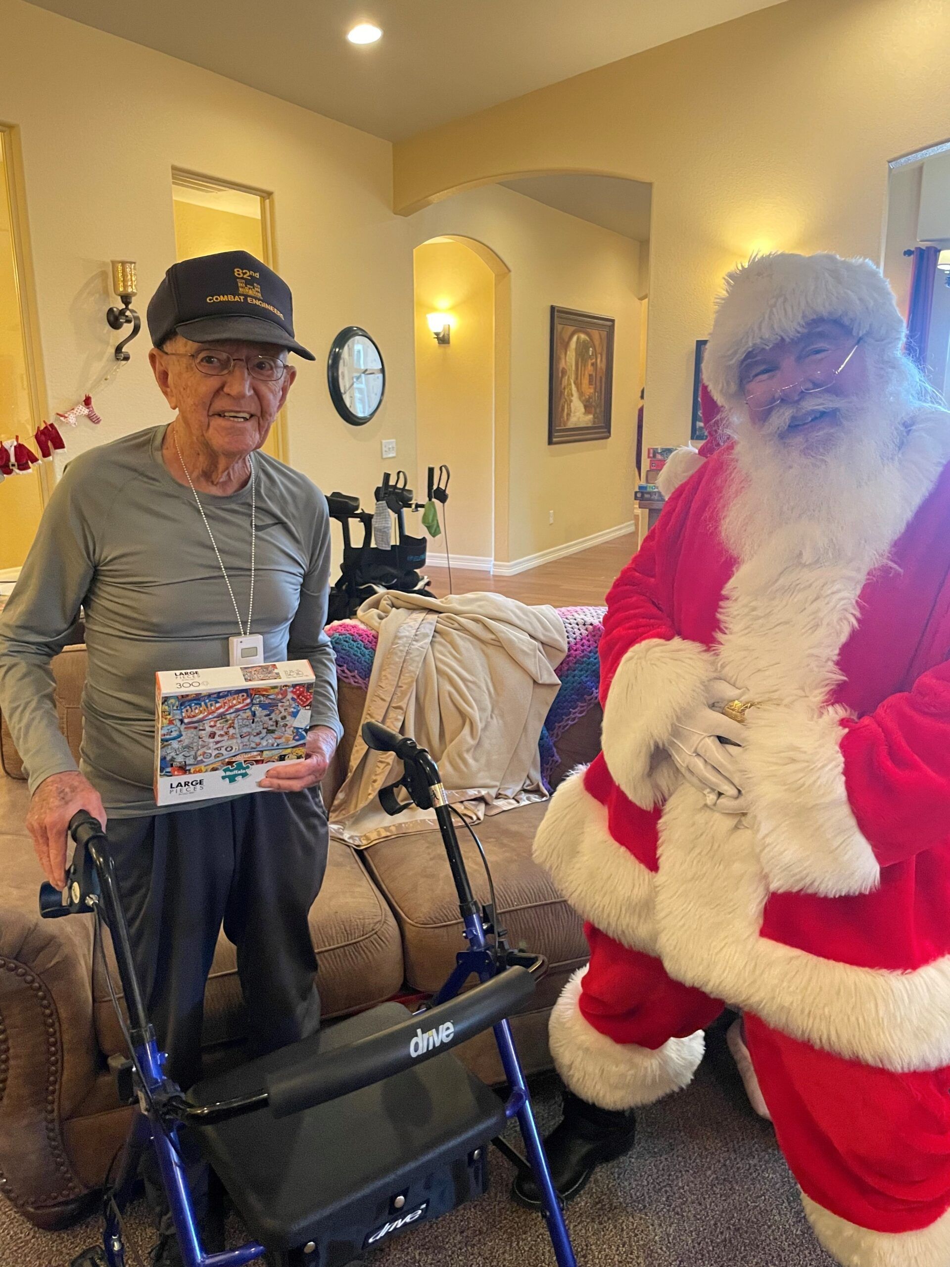 A man in a walker is standing next to santa claus in a living room.