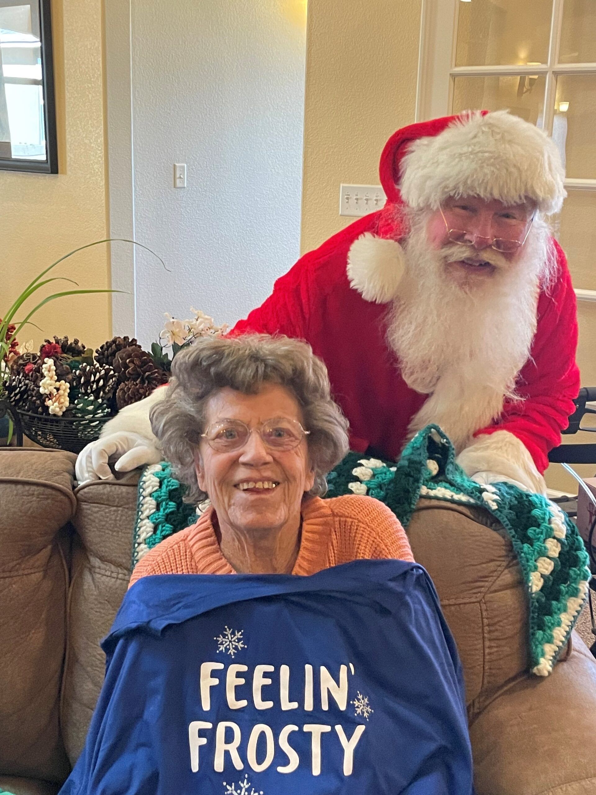 A woman wearing a sweater that says feelin frosty is sitting on a couch next to santa claus